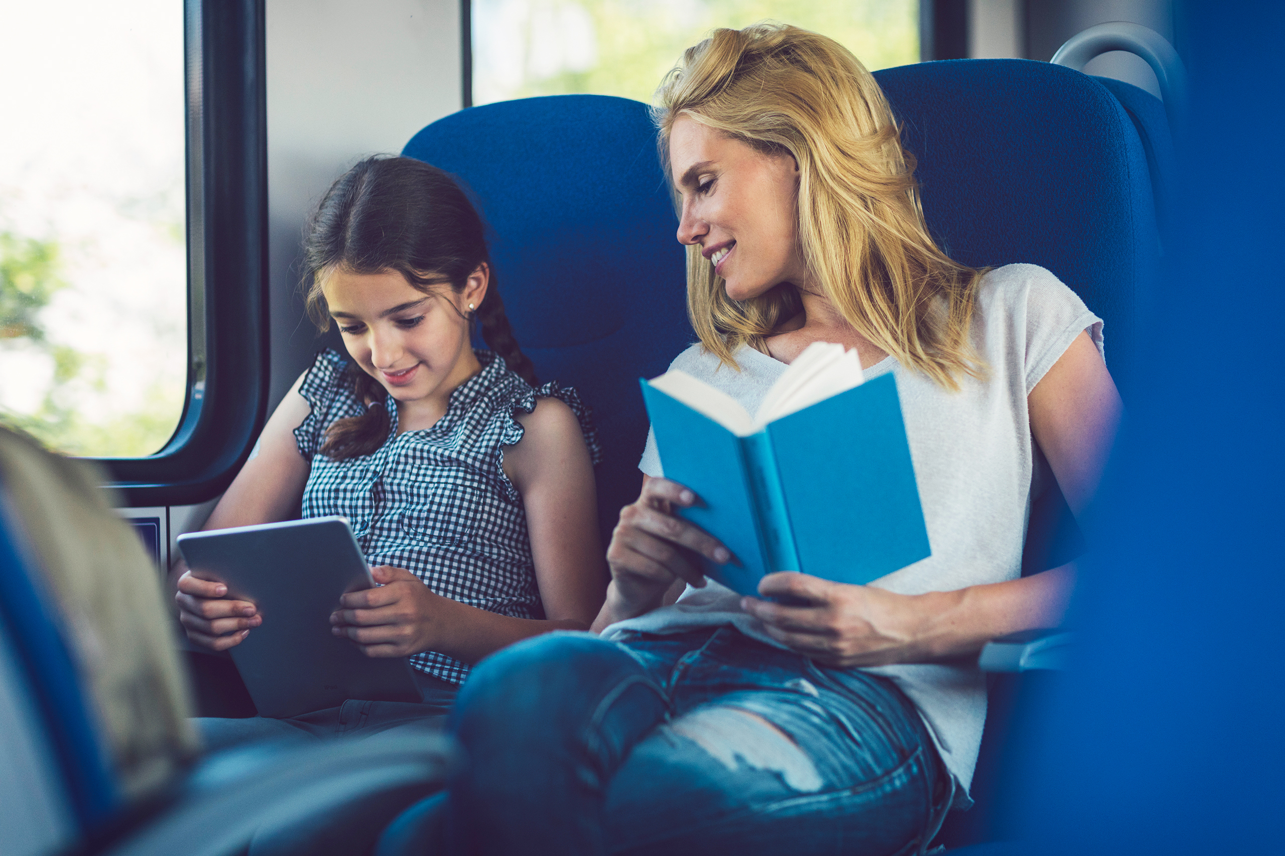 Kind met tablet en moeder met boek samen op de trein